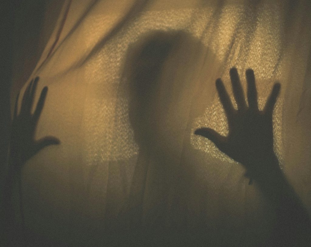 WHEN PARTY COLOURS BECOME SHIELDS FOR WRONGDOING Silhouette of a person with hands pressed against a fabric curtain, creating a mysterious shadow.