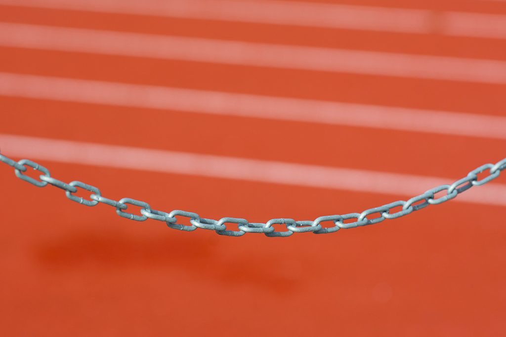 Detailed close-up of a metal chain against a vibrant red running track background.