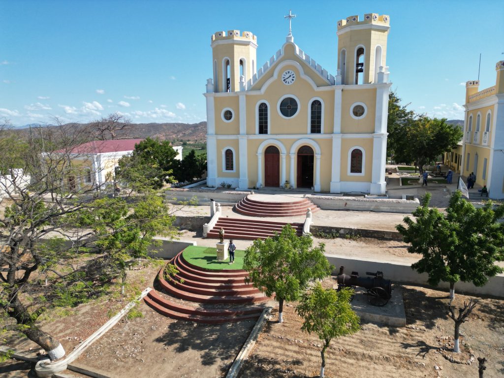 WHY DO PEOPLE FIGHT TO LEAD A CHURCH? Aerial view of a historic church in Deghe, Mozambique, surrounded by trees and sunny landscapes.