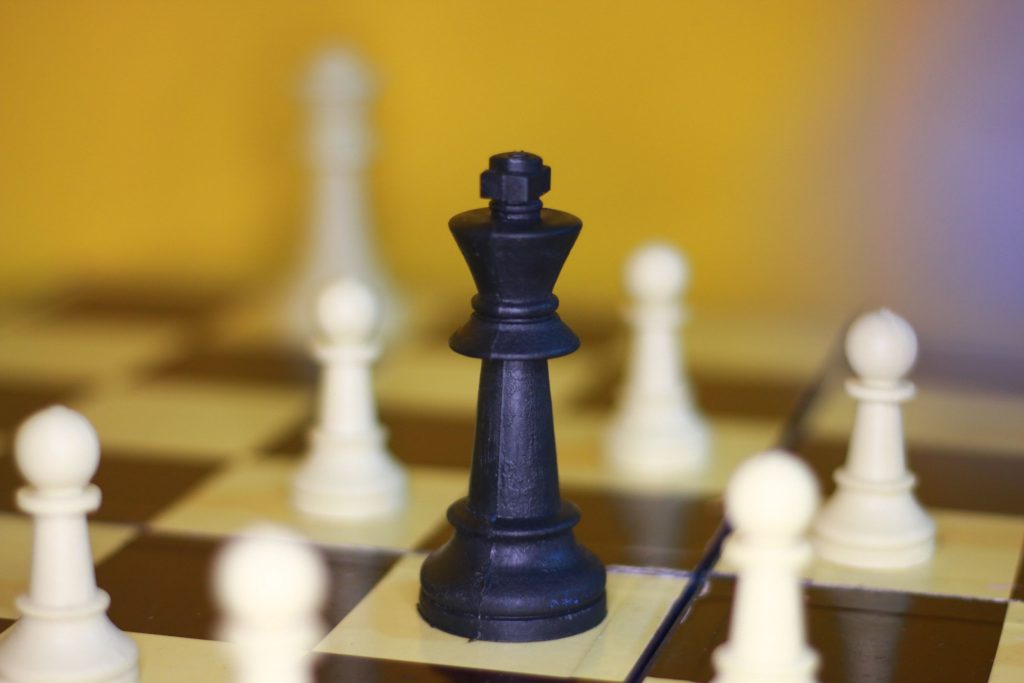 Leadership Destroys the Person Who Is Not Prepared to Lead. A focused shot of a black king chess piece surrounded by white pawns on a chessboard.
